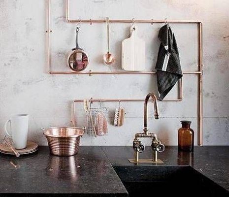 Las tuberías de cobre están dispuestas de manera decorativa en una pared de la cocina, sirviendo como almacenamiento para utensilios, con un juego de fregadero y