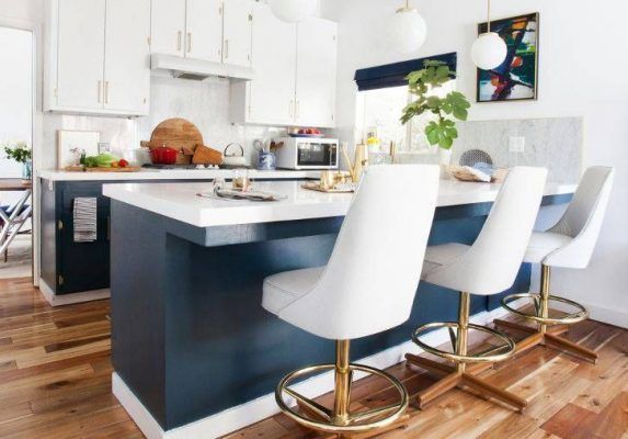 Una moderna cocina americana con gabinetes blancos, una isla azul con encimera de mármol y sillas blancas con bases doradas.