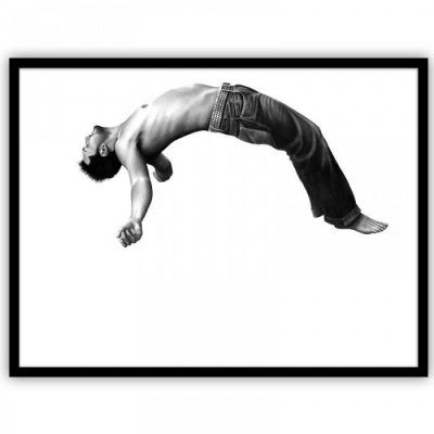 Una fotografía en blanco y negro de un hombre sin camiseta suspendido en el aire de forma horizontal, con los brazos extendidos y las piernas estiradas, sobre un fondo blanco que lo diferencia.