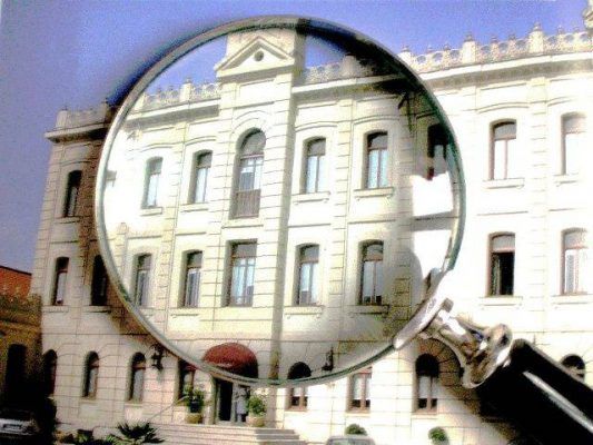 Una inspección técnica de edificios realizada mediante una lupa sostenida contra el fondo de un edificio arquitectónico clásico, con la lente distorsionada.