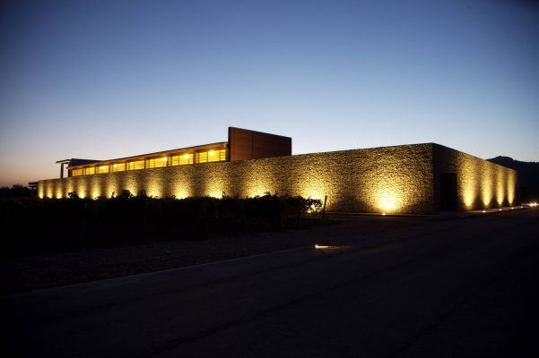 Una moderna bodega en Benissalem, Mallorca, iluminada al atardecer con luces exteriores que proyectan un cálido brillo en sus paredes texturizadas.