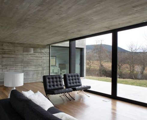 Un espacio moderno con un elegante sofá de cuero negro estilo Barcelona con una otomana a juego, un sofá tapizado en gris y una mesa auxiliar cilíndrica blanca hecha con materiales de contenedores de bienestar.