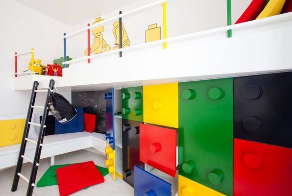 Una habitación infantil con una litera temática de Lego colorida, que cuenta con compartimentos de almacenamiento y un tobogán, incluyendo una escalera para acceder a