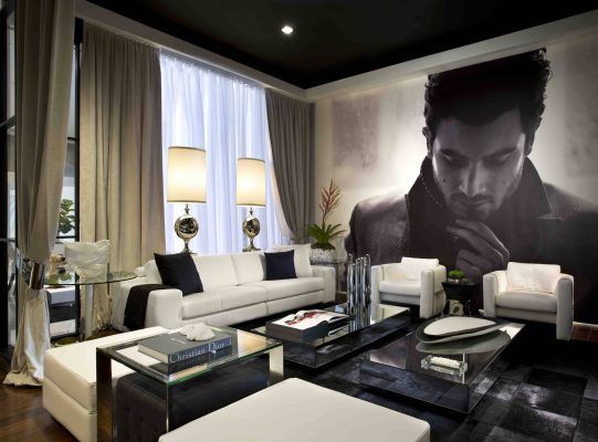 Una sala de estar moderna con un gran retrato en escala de grises en la pared, que presenta una fotografía de gran tamaño del rostro de un hombre. La habitación incluye un sofá blanco, dos sillones, una mesa de café y