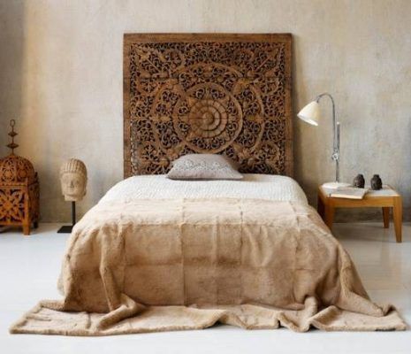 Un dormitorio minimalista con un enfoque decorativo Feng Shui, que incluye un cabecero de madera ornamentado, ropa de cama neutra, una mesa auxiliar sencilla y elementos decorativos que reflejan un estilo rústico o étnico para favorecer un mejor descanso.