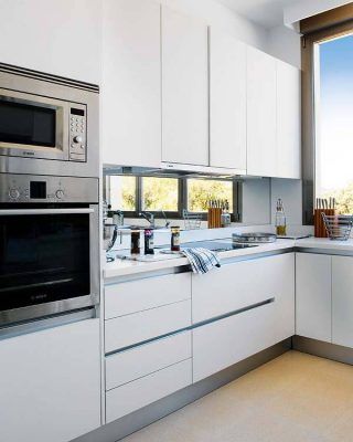 Una cocina moderna con gabinetes blancos, electrodomésticos de acero inoxidable y una ventana sobre el fregadero que ofrece una vista al exterior, diseñada para