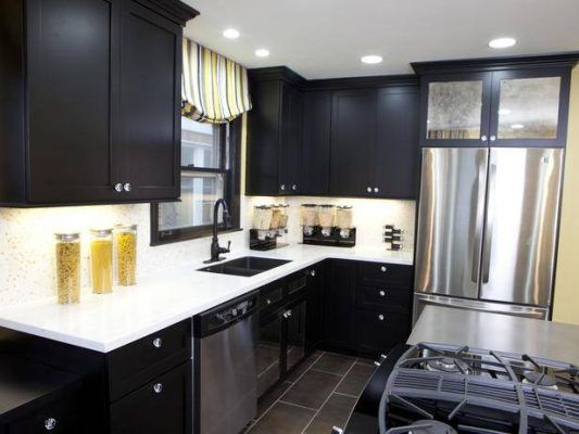 Una cocina moderna con gabinetes negros, encimeras blancas, electrodomésticos de acero inoxidable y una cortina de ventana estampada amarilla y