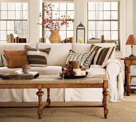 Una acogedora sala de casa con un sofá blanco adornado con cojines decorativos, una mesa de café de madera con libros y velas, flanqueada por