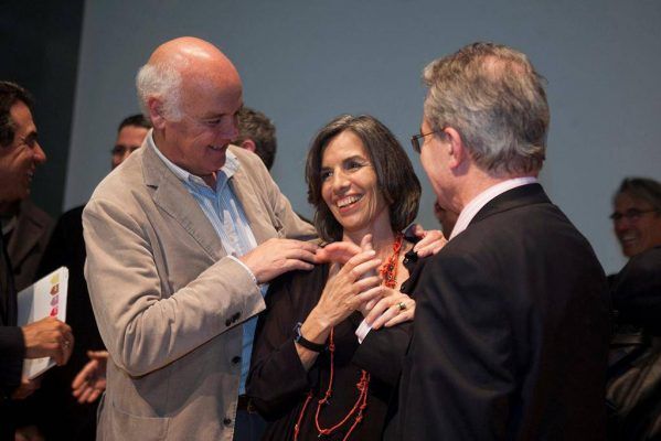 Tres personas entablaron una agradable conversación, con la nueva presidenta en el centro sonriendo mientras un hombre ajusta su collar y otro observa la interacción riendo.
