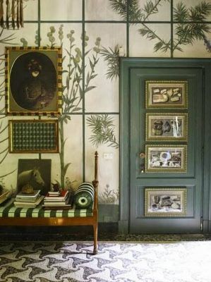 Una entrada de estilo vintage con papel tapiz botánico, una puerta verde oscuro adornada con arte enmarcado, un banco de madera con libros y un bastón decorativo.