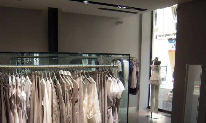 Una vista interior de una tienda de ropa, diseñada por un interiorista profesional, con una gama de prendas colgadas en un perchero y un maniquí vestido.