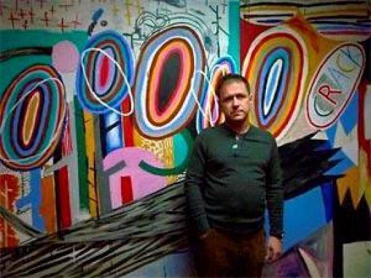 Un hombre se para frente a una colorida pintura abstracta de Abraham Lacalle, que presenta patrones audaces y arremolinados y formas geométricas.