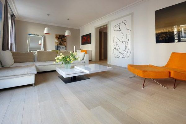 Moderna sala de estar con paredes neutras, un sofá blanco, una silla vibrante naranja, una mesa de café blanca, arte contemporáneo y decoración del